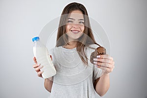 Young beautiful fit woman holding bottle with milk in one hand and chocolate cookies in another looking hungry healthy lifestyle