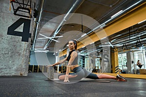 Young beautiful fitness woman in sportswear sitting on yoga mat at gym, looking at camera while working out alone