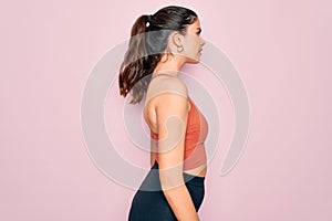 Young beautiful fitness woman wearing sport excersie clothes over pink background looking to side, relax profile pose with natural