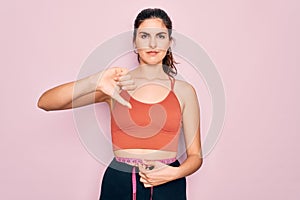 Young beautiful fitness woman wearing sport excersie clothes using measuring tape with angry face, negative sign showing dislike