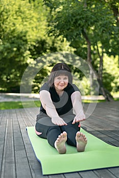 Young beautiful flexible girl makes a lean forward with her hands from a sitting position. Stretching exercises for beginners