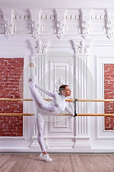 Young beautiful flexible girl in white jumpsuit is posing in a dance studio. Stretching and body ballet theme. Modern dance trend