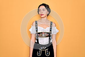 Young beautiful german woman with blue eyes wearing traditional octoberfest dress smiling looking to the side and staring away