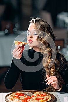 Young beautiful girl alone eating pizza in a restaurant.