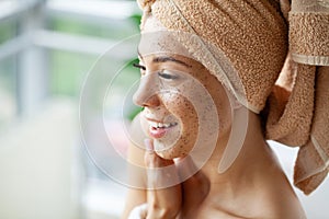 Young beautiful girl applying facial scrub mask on skin.