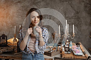 The young beautiful girl the artist with a tea cup in the workshop. Reflects on images for the future pictures. Creative