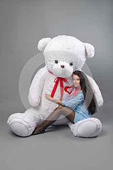 Young beautiful girl with big teddy bear soft toy happy smiling and playing on grey background