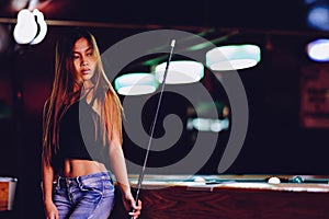 Young beautiful girl in a billiard club, with cue stick posing