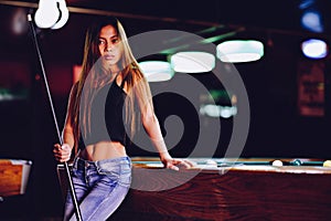 Young beautiful girl in a billiard club, with cue stick posing