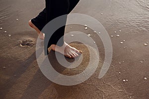 Young beautiful girl in black clothes walking on the beach. She walks along shore. A walk at sunset. Nobody around