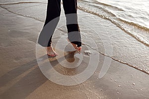 Young beautiful girl in black clothes walking on the beach. She walks along shore. A walk at sunset. Nobody around