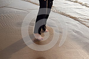 Young beautiful girl in black clothes walking on the beach. She walks along shore. A walk at sunset. Nobody around