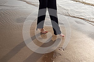 Young beautiful girl in black clothes walking on the beach. She walks along shore. A walk at sunset. Nobody around