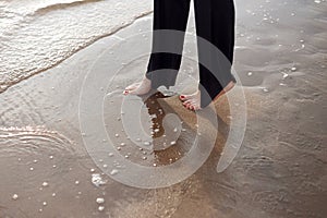 Young beautiful girl in black clothes walking on the beach. She walks along shore. A walk at sunset. Nobody around