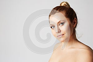 Young beautiful woman with blonde hair fixed behind, big eyes, thick eyebrows and naked shoulders smiling on gray