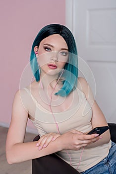 Young beautiful girl with blue hair is using a smartphone with headphones.