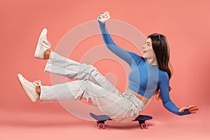 A young beautiful girl in a blue jacket and denim pants with a mini skateboard on a pink background