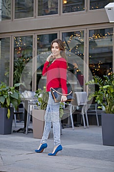 Young beautiful girl in blue jeans and red shirt on the background of summer street