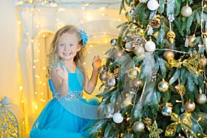 Young beautiful girl in blue white elegant evening dress sitting on floor near christmas tree and presents on a new year