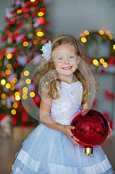 Young beautiful girl in blue white elegant evening dress sitting on floor near christmas tree and presents on a new year