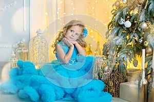 Young beautiful girl in blue white elegant evening dress sitting on floor near christmas tree and presents on a new year
