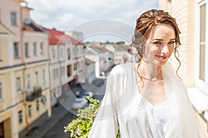 Young beautiful girl bride in a peignoir standing on the balcony overlooking the old town and waiting for the groom
