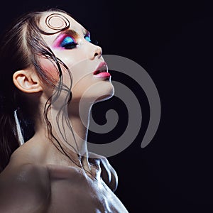 Young beautiful girl bright makeup with a wet look shine, dark background