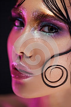 Young beautiful girl bright makeup with a wet look shine, dark background, pink light, disco style