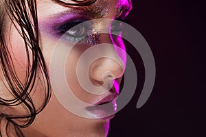 Young beautiful girl bright makeup with a wet look shine, dark background. Profile close-up