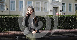 Young beautiful girl in casual clothes sitting on a bench and talking on mobile phone.