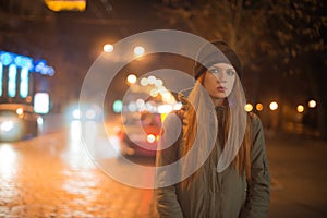 Young beautiful girl catches a taxi in the city street at night