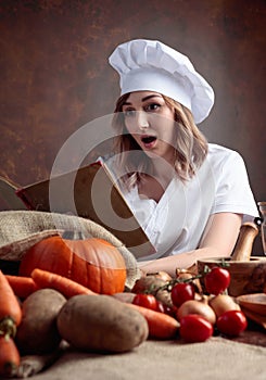 Young beautiful girl in a chef`s uniform reads an old cookbook.