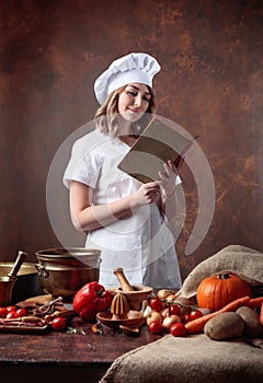 Young beautiful girl in a chef`s uniform reads an old cookbook.