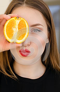 Young beautiful girl closeup portrait with orange fruit, red lipstick and perfect makeup