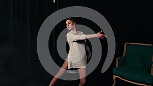 Young beautiful girl dancing contemporary in a dark room with a green chair.