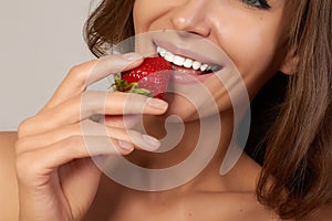 Young beautiful girl with dark curly hair, bare shoulders and neck, holding strawberry to enjoy the taste and are dieting,