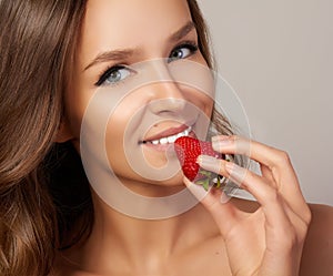 Young beautiful girl with dark curly hair, bare shoulders and neck, holding strawberry to enjoy the taste and are dieting,