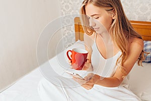 Young beautiful girl drinking coffee, sitting in bed and looking
