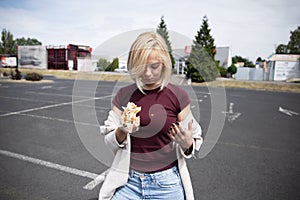 Young beautiful girl eating hot dog in the parking lot.