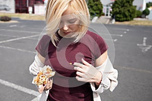 Young beautiful girl eating hot dog in the parking lot.