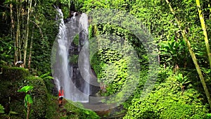 Young beautiful girl enjoy the scenic view of the waterfall Munduk on a background tropical nature island Bali