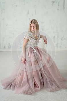 Young beautiful girl in an evening dress with lace and pink fartine on the background of a white textural wall.