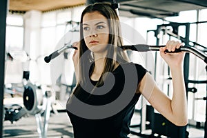 Young beautiful girl exercising in the fitness gym, with lat machine