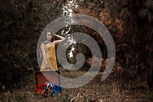 Young beautiful girl in the forest is posing with a retro suitcase in her hands.