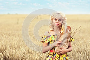 Young beautiful girl with a full pack of bread in a field with ripe wheat. Model posing against a background of crops