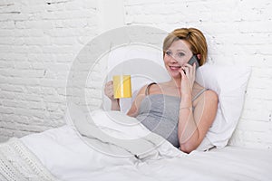 Young beautiful girl having coffe on bed while watching internet news in his mobile phone in online communication