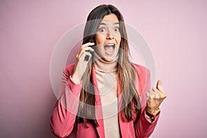 Young beautiful girl having conversation talking on the smartphone over white background screaming proud and celebrating victory