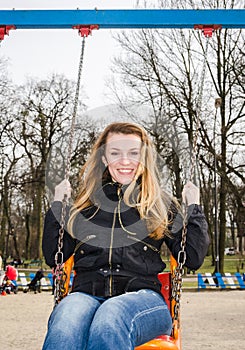 Young beautiful girl having fun riding a chain-swing in the park