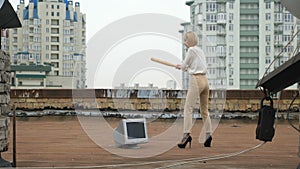 Young beautiful girl in high heels smashes the monitor with a bat. Bat, violence, hatred, anarchy, destruction, roof. 60