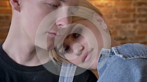 Young beautiful girl hipster is laying on her boyfriend`s shoulder, relationship conception, brick background